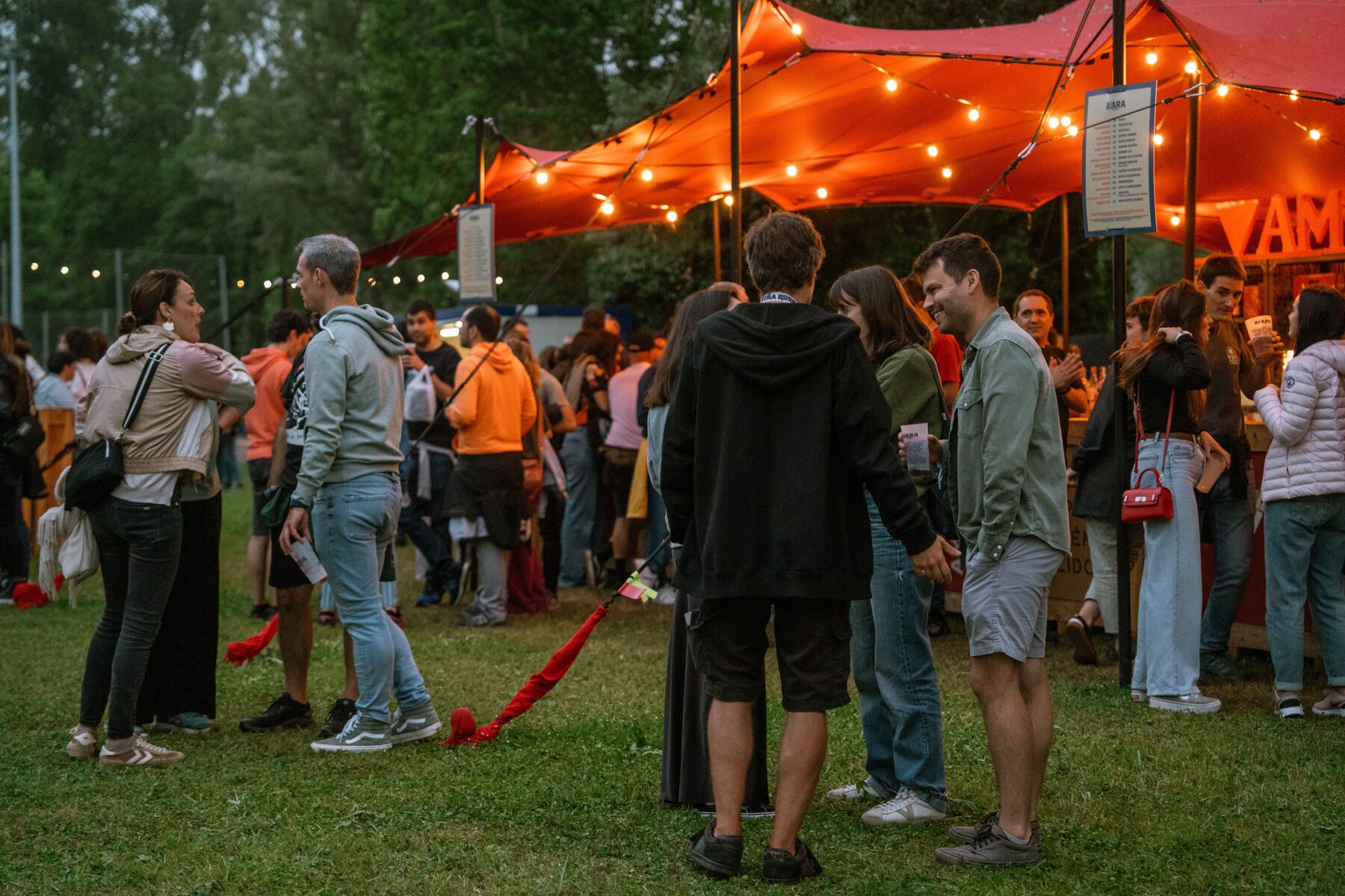 Scène de festival en extérieur avec public nombreux au coucher du soleil, ambiance culturelle et lumineuse